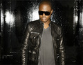 Person mit Sonnenbrille und schwarzer Lederjacke steht vor dunklem Hintergrund, schaut nach vorne.