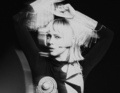 Schwarz-weiß-Bild einer Person mit kurzem, blondem Haar, die Arme erhoben. Bewegungsunschärfe und ein futuristisches Outfit.