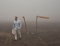 Ein Mann geht durch eine neblige Landschaft, neben ihm ein Schild mit der Aufschrift 'Heitissandu 20'.