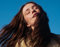 Person mit langen Haaren schließt die Augen, lehnt den Kopf leicht zurück. Hintergrund ist ein klarer blauer Himmel.