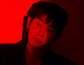 Porträt eines nachdenklichen Menschen in rotem Licht, schwarzer Hintergrund. Die Person trägt Ohrringe und blickt leicht nach unten.
