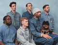 Sechs Männer in blauer Jeanskleidung, einer hält einen kleinen Hund. Sie stehen und sitzen vor einem blauen Hintergrund.
