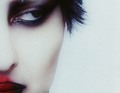 Nahaufnahme eines Gesichts mit dramatischem Make-up in dunklen Tönen und roten Lippen auf heller Haut, scharfes Licht.