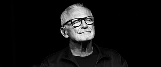 Ein älterer Mann mit Brille und Bart schaut nachdenklich in die Ferne. Das Bild ist in Schwarz-Weiß gehalten.