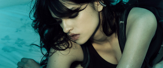 Junge Person mit dunklem Haar und Piercing blickt nachdenklich zur Seite. Der Hintergrund ist in Blau- und Grüntönen gehalten.