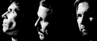 Drei Männer im Profil, in schwarz-weiß beleuchtet, schauen in verschiedene Richtungen. Ein dramatisches, schattenreiches Bild.