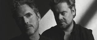 Zwei Männer in Schwarz-Weiß, einer schaut direkt in die Kamera, der andere blickt leicht zur Seite. Licht-Schatten-Effekt.