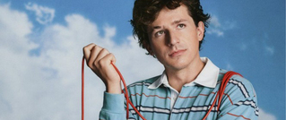 Eine Person in gestreiftem Hemd hält ein rotes Kabel, vor einem Hintergrund mit blauem Himmel und weißen Wolken.