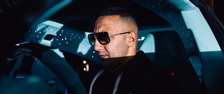 Ein Mann mit Sonnenbrille sitzt in einem Auto. Die Innendecke ist mit kleinen Lichtern verziert, die Sterne imitieren.