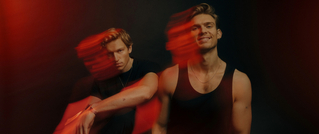 Zwei Personen mit Bewegungsunschärfe vor schwarzem Hintergrund, umgeben von rotem Licht. Sie tragen schwarze Oberteile.