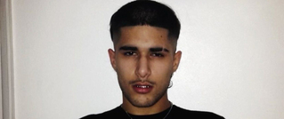 Ein junger Mann mit dunklem, kurzem Haar, trägt ein schwarzes T-Shirt und eine Halskette. Der Hintergrund ist weiß.