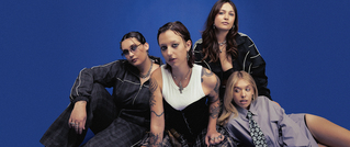 Vier Personen posieren vor einem blauen Hintergrund. Sie tragen modische Kleidung und haben verschiedene Posen eingenommen.