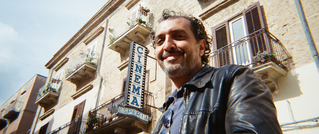 Ein lächelnder Mann steht vor einem alten Gebäude mit einem Schild CINEMA ESperia.