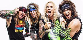 Vier Mitglieder einer Rockband posieren energisch. Sie tragen bunte Kleidung, Bandanas und haben E-Gitarren. Alle haben lange Haare und ausdrucksstarke Gesichtsausdrücke.