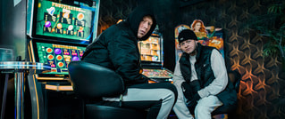 Zwei Personen in Sportkleidung sitzen vor leuchtenden Spielautomaten in einem dunklen Raum.