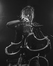 Ein Musiker spielt energetisch ein Musikinstrument auf der Bühne in einem schwarz-weißen, stimmungsvoll ausgeleuchteten Setting.