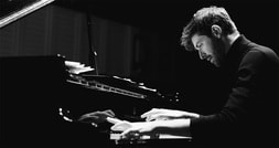 Ein Mann spielt konzentriert Klavier. Das Bild ist in Schwarz-Weiß gehalten, die Beleuchtung betont seine ruhige, fokussierte Haltung.