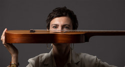 Eine Person hält eine Gitarre horizontal vor ihr Gesicht, sodass nur die Augen oberhalb des Instruments sichtbar sind.