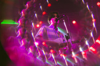 Ein Musiker singt und spielt Gitarre auf der Bühne, umgeben von bunten Lichtern und einem kaleidoskopartigen Effekt.