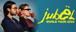 Zwei Personen mit Sonnenbrillen trinken Cocktails. Text: 'jubël WORLD TOUR 2022' in gelber Schrift auf blauem Hintergrund.