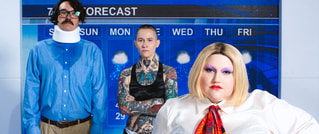 Drei Personen stehen vor einer Wetterkarte. Eine Person trägt eine Halskrause, eine hat Tätowierungen, eine trägt auffälliges Make-up.