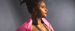 Frau im Profil vor grauem Hintergrund trägt einen pinken Schal, große Ohrringe und hat hochgesteckte Haare.