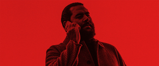 Eine Person mit Bart telefoniert und trägt einen Mantel. Das Bild ist in einem Rotfilter gehalten.