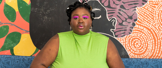 Person in einem neon-grünen Top sitzt vor einer bunten, künstlerischen Wand, verziert mit abstrakten Mustern und Gesichtern.