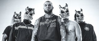 Fünf Personen posieren in Sportkleidung, vier tragen kunstvolle Wolfsmasken. Der Mann in der Mitte zeigt Tattoos und ein ärmelloses Shirt.