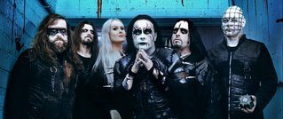 Sechs Menschen in dunkler Kleidung mit dramatischem Make-up und Gesichtsbemalung stehen vor einem blauen Hintergrund.